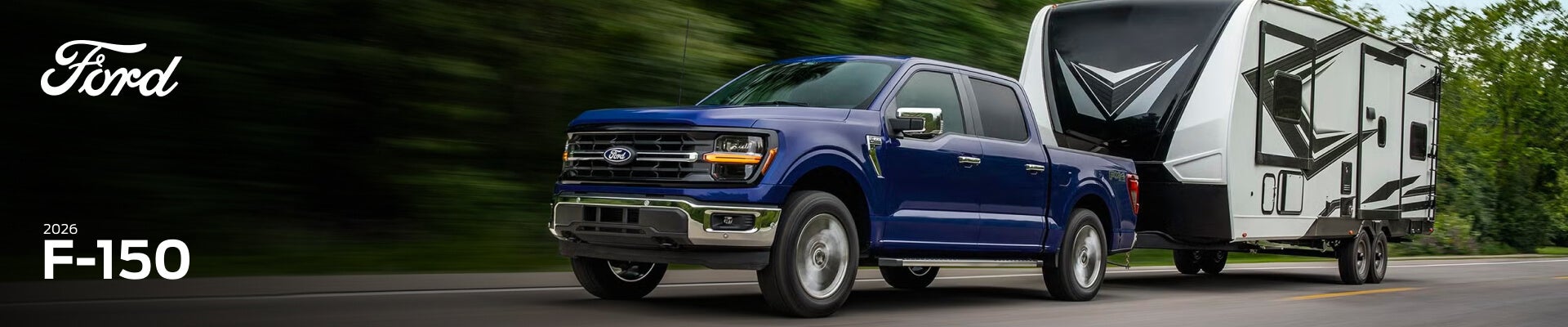 Exterior side view of a blue 2026 Ford F-150 towing a camper trailer down a remote forest highway.