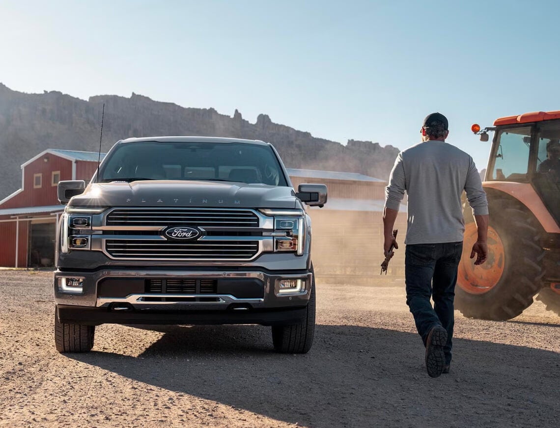 Exterior low angle shot of a Ford F-150 parked on a farm as a man walks near a tractor nearby.