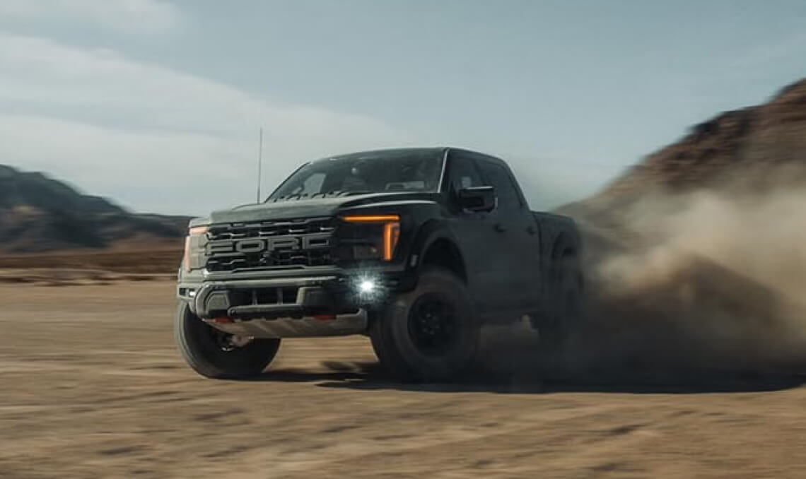 A black 2026 Ford F-150 kicking up sand while offroading in a desert clearing.